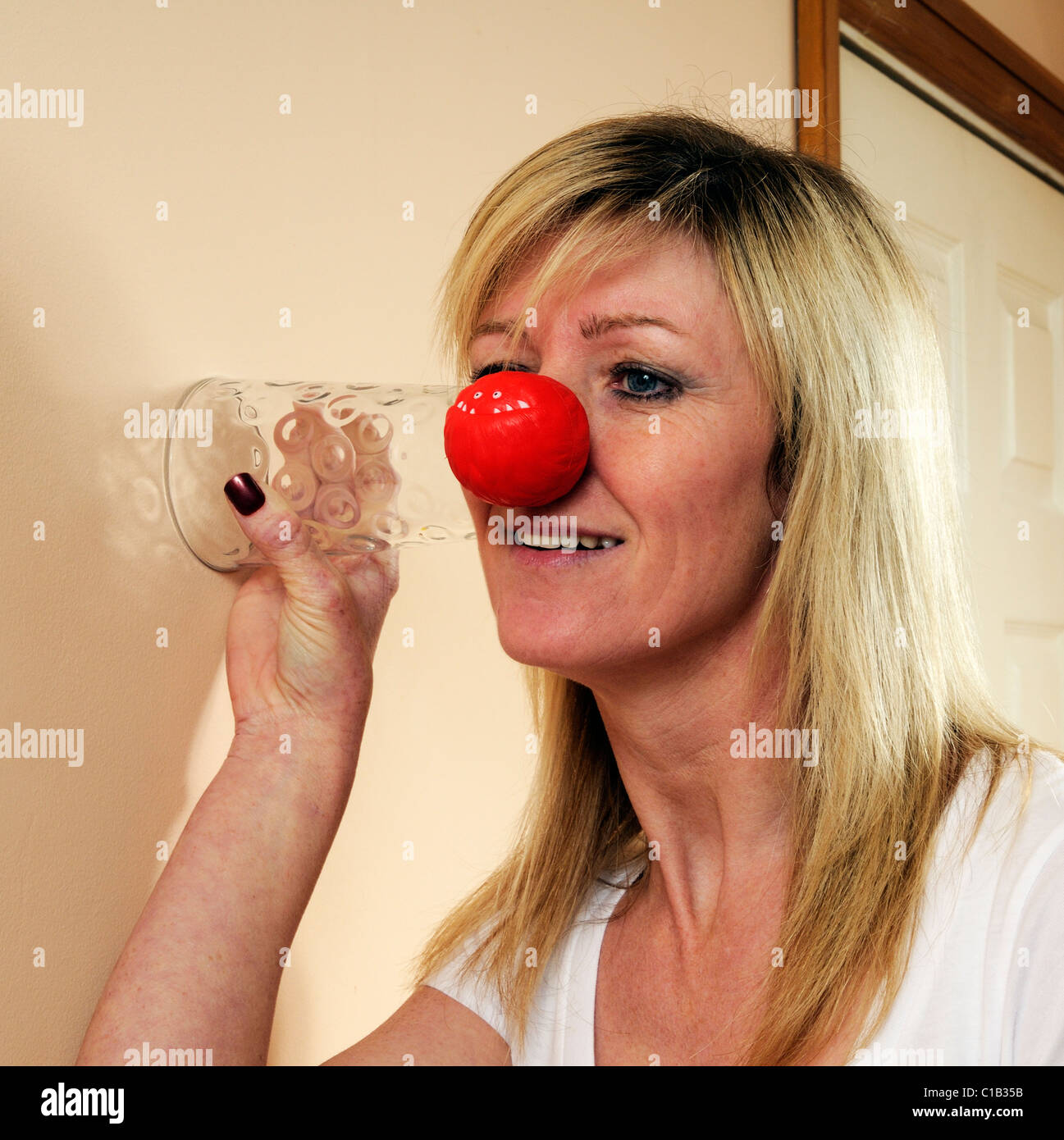 woman-wearing-a-red-nose-uses-a-glass-tumbler-as-a-listening-device-C1B35B.jpg